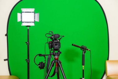 Kameranın tripod, led projektör, kulaklık ve bir yönlü mikrofon yeşil bir arka plan üzerinde. Chroma anahtar. Yeşil ekran