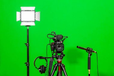 Kameranın tripod, led projektör, kulaklık ve bir yönlü mikrofon yeşil bir arka plan üzerinde. Chroma anahtar. Yeşil ekran