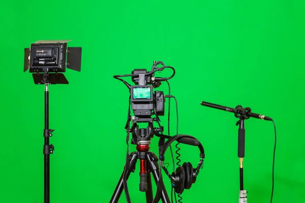 A câmera no tripé, levou holofotes, fones de ouvido e um microfone direcional em um fundo verde. A chave chroma. Tela verde — Fotografia de Stock