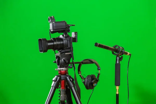 Câmera de vídeo em um tripé, fones de ouvido e um microfone direcional em um fundo verde. A chave chroma. Tela verde — Fotografia de Stock