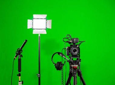 Kameranın tripod, led projektör, kulaklık ve bir yönlü mikrofon yeşil bir arka plan üzerinde. Chroma anahtar. Yeşil ekran.