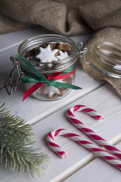 Glazen pot met kerstkoekjes en snoep stokken op een witte houten tafel. — Stockfoto