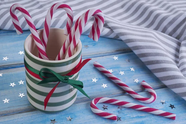 Striped ceramic cup with candy canes on a blue wooden table. — Stock Photo, Image