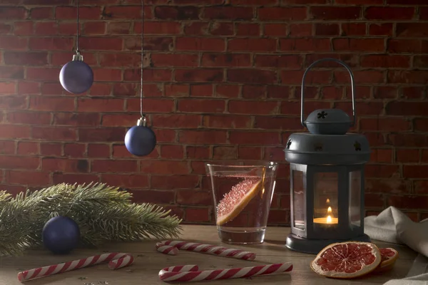 Koktél Grapefruit, gyertya, karácsonyi játékokat és édességet vesszők, egy vörös téglából épült a fenyő ága — Stock Fotó