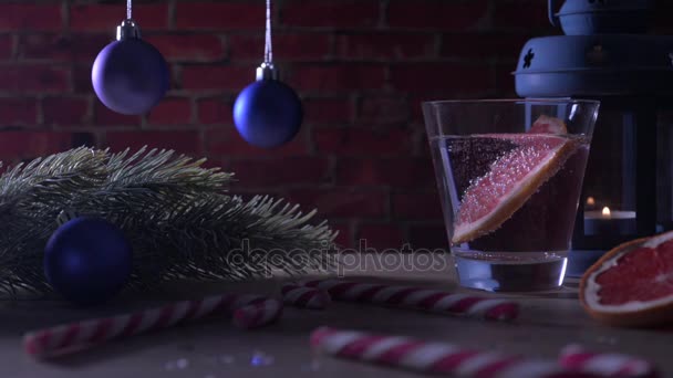 Cocktail Pompelmo, candela, ramo di abete con giocattoli di Natale e bastoncini di zucchero su un mattone rosso — Video Stock