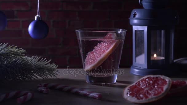 Cocktail Grapefruit, kaars, tak van de zilverspar met Kerstmis speelgoed en snoep stokken op een rode baksteen — Stockvideo