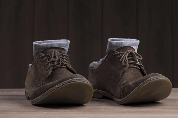 Brown suede shoes with brown laces and grey socks on the background of dark natural wood.
