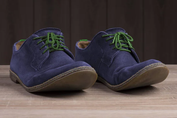 Modré semišové boty s zelené tkaničky na pozadí tmavého přírodního dřeva. — Stock fotografie