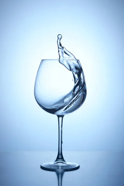 Splash de água azul em um copo em um fundo azul escuro com reflexão — Fotografia de Stock