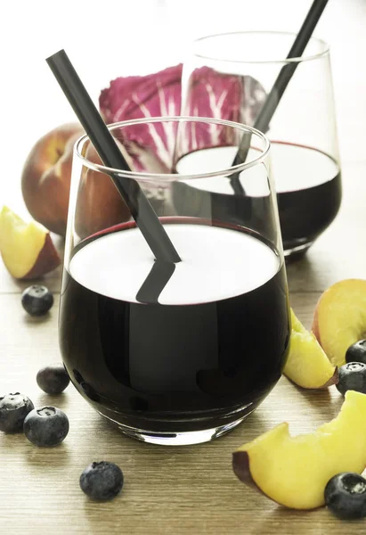 Черничный сок в прозрачном красивом стакане с персиками и красным листом на деревянном столе . — стоковое фото