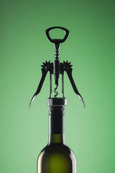 緑の背景にオープニングのスタイリッシュなコルク抜きでワインのボトル. — ストック写真