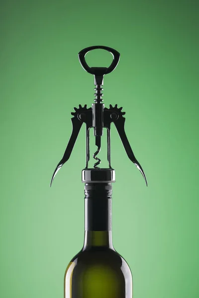 Una botella de vino con un sacacorchos elegante para abrir sobre un fondo verde . — Foto de Stock