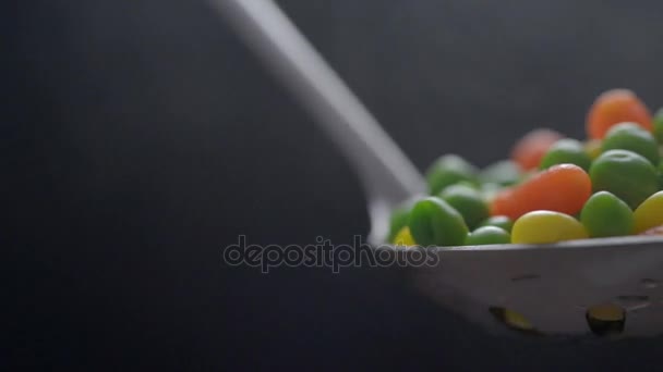 Ervilhas verdes fervidas, milho e cenoura em uma concha com vapor em um fundo azul escuro . — Vídeo de Stock