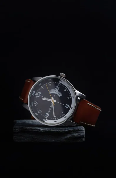 Relógio de pulso com um mostrador preto em uma pedra cinza com um fundo escuro . — Fotografia de Stock