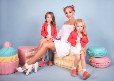 Şirin çocuklar, iki küçük kız eğleniyor ve mavi bir arka planda oynuyorlar, tatlıya bayılıyorlar: Pasta, çörek, tatlı ve kurabiye! Çocukların parlak giysileri vardır, gülerler. Sarılmak ve sevmek, iki ikiz kardeş ve güzel bir kızın annesi.