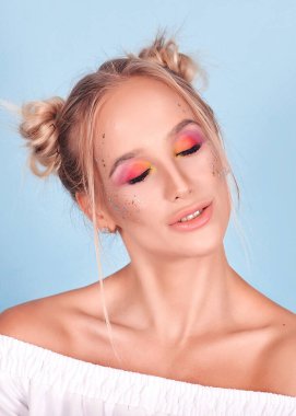 Parlak, alışılagelmedik makyajlı ve iki külahlı, çok tatlı tatlı şeker kız zıplayan, eğlenen ve gülen kız. Bu mavi arka planda bir bayan. Yanında büyük turtalar ve çörekler var. Makaronların portresi.