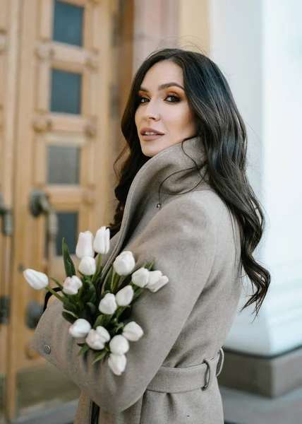 Gülücükler saçan güzel bir kız, gülen çiçeklerle, güneşli havada sokakta portre, lalelerle mutlu kahve içmek, kahkahalar atan bir kitap okumak, bahar mevsiminde makyajlı, ince bir palto giymiş, şık bir mankenle.