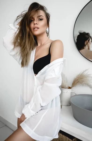 Güzel bir genç kız, banyoda güneşleniyor, beyaz bir gömlek içinde, sabah seksi, fotoğrafta açık renk narin kahverengi gözler, masada oturuyor, sandalye, yerde, ışık, moda, dergi, gülümseme.