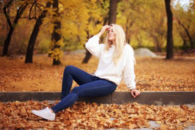 İki güzel sarışın kız gülerek ve eğlenerek sonbahar parkında yürüyorlar, sonbahar yapraklarını fırlatıyorlar, telefonda fotoğraf çekiyorlar, halsiz stil, şirin portre, mesafeye düşünceli bir bakış, nazik gülümseme, gençlik ve hafiflik, kız arkadaşlar ve kız kardeşler