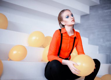 İri mavi gözlü nazik sarışın bir kız. Ev fotoğrafı, portre. Genç ve çekici. Boncuklar, inciler ve tüyler. Sabahlık giymiş bir kız, güneşli bir gün, sıcak ve sıcak bir evde. Alışılmadık parlak makyaj, gelin buketi, çiçekler, bahar