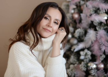 Süslü bir Noel ağacının arka planında süveter giyen ev tarzı güzel bir kız.