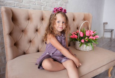 Çiçeklerle ve lalelerle çevrili şapkalı ve narin elbiseli küçük tatlı bir kız.