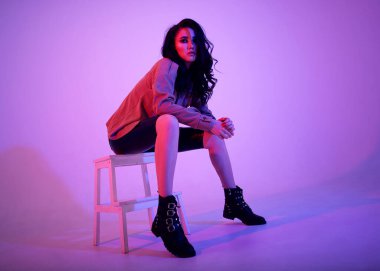 Parlak esmer Asyalı kız neon ışıklı pembe ve mor renkli şık elbiseli.