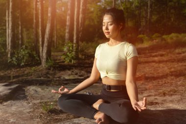 Genç ve güzel Asyalı kadın yoga yapıyor ve dışarıda meditasyon yapıyor.
