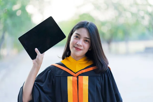 Young Cheerful Beautiful Female Gradute Wearing Academic Gown Holding Tablet — Stock Photo, Image