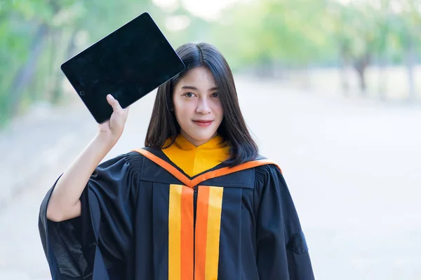 Young Cheerful Beautiful Female Gradute Wearing Academic Gown Holding Tablet — Stock Photo, Image