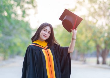 Kolej kampüsündeki ilk gününde elinde akademik elbise şapkası olan genç ve neşeli bir kızın portresi..