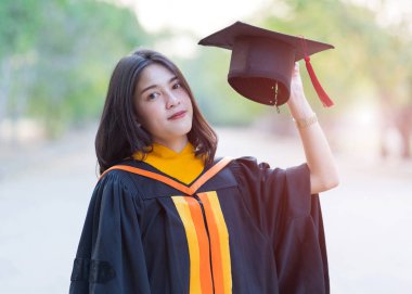 Kolej kampüsündeki ilk gününde elinde akademik elbise şapkası olan genç ve neşeli bir kızın portresi..