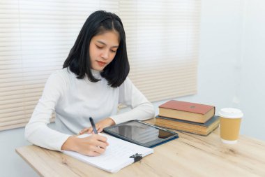 Neşeli Asyalı kız öğrenci üniversite kütüphanesinde kendi kendine öğrenim görüyor ödevini yapmak ve sınava hazırlanmak için..