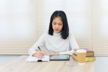 Neşeli Asyalı kız öğrenci üniversite kütüphanesinde kendi kendine öğrenim görüyor ödevini yapmak ve sınava hazırlanmak için..