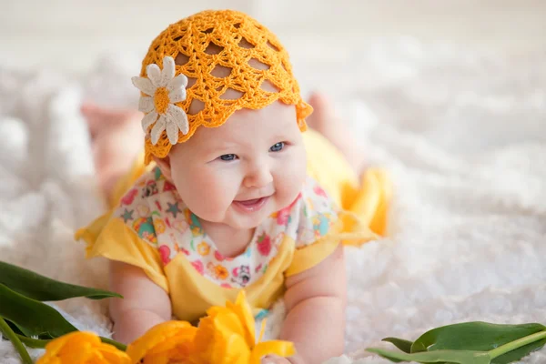Niña en un vestido amarillo y un sombrero amarillo de ganchillo acostado en la cama con tulipanes amarillos —  Fotos de Stock
