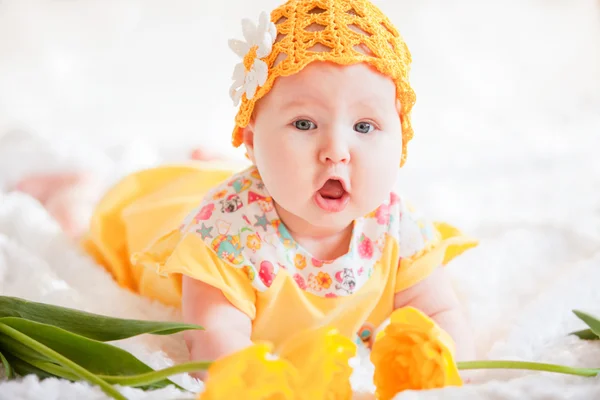 Menina em um vestido amarelo e um chapéu amarelo de malha deitado na cama com tulipas amarelas — Fotografia de Stock