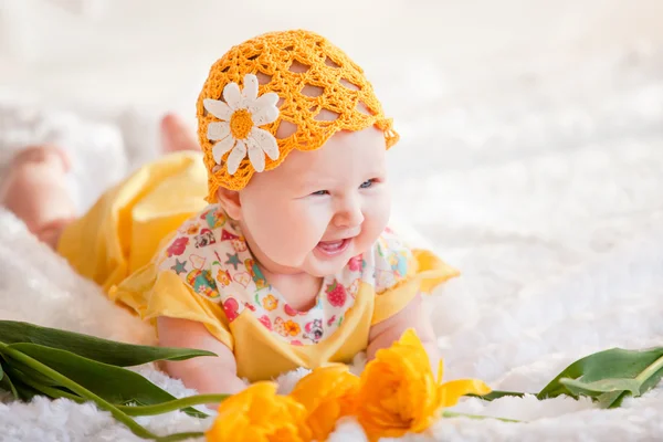 Niña en un vestido amarillo y un sombrero amarillo de ganchillo acostado en la cama con tulipanes amarillos —  Fotos de Stock
