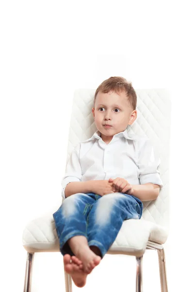 En pojke sitter på en vit bakgrund på en vit stol — Stockfoto