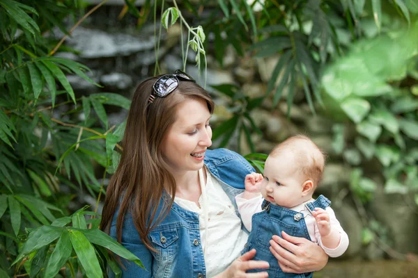 Joyeux jeune femme tenant un bébé lors d'une promenade dans le parc — Photo