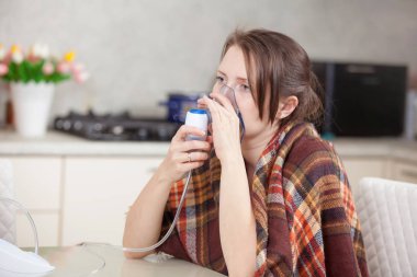 Young woman doing inhalation with a nebulizer at home clipart