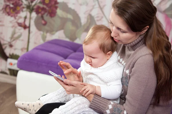 Ung kvinna med ett barn ser till en smartphone. — Stockfoto