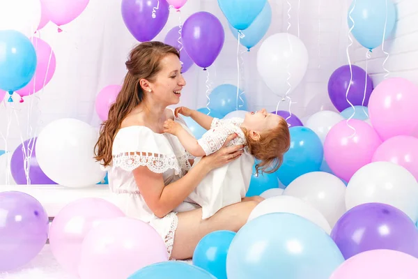 Ευτυχισμένη μητέρα αγκαλιάζει την κόρη της γύρω από μια παρτίδα χρωματιστά μπαλόνια απομονωμένη σε λευκό. — Φωτογραφία Αρχείου