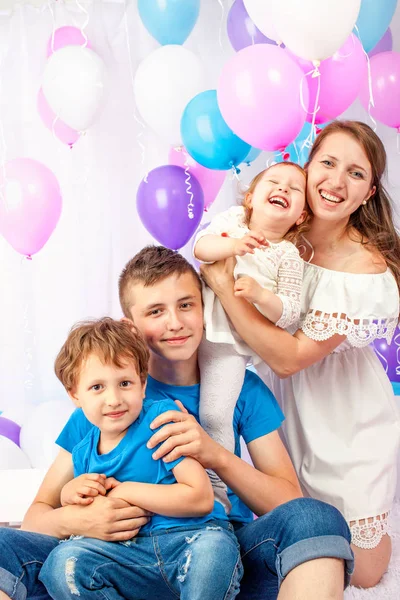 Ευτυχισμένη μητέρα αγκαλιάζει τα τρία παιδιά της γύρω από μια παρτίδα από πολύχρωμα μπαλόνια, χαμογελαστά παιδιά. απομονωμένα σε λευκό. — Φωτογραφία Αρχείου