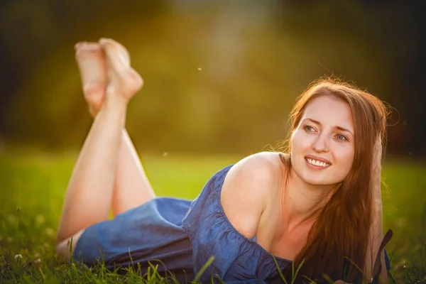 Beautiful girl lying on green grass in the Park in the evening at sunset — Stock Photo, Image