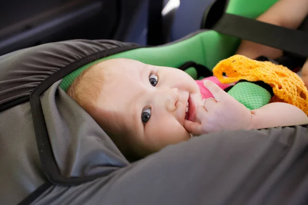 A little girl is holding in his mouth a finger lying in the car seat — Stock Photo, Image