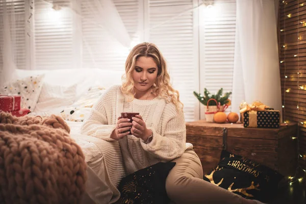 Ragazza bionda in maglione con una tazza di tè seduta sul letto — Foto Stock