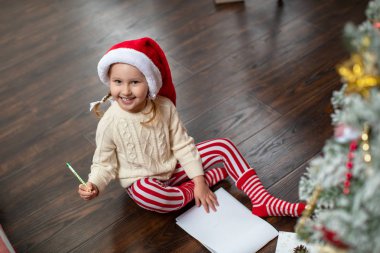 Küçük bir çocuk yılbaşının önünde yerde oturuyor.