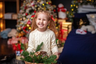 Küçük bir kız elinde bir sepet süs ve çelenk ile gülümsüyor.