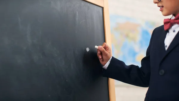 かわいい陽気な少年はチョークで黒板に書きます コピースペース 学校のスーツを着た7歳の少年は テキストのための自由なスペースの前に点を置きます — ストック写真