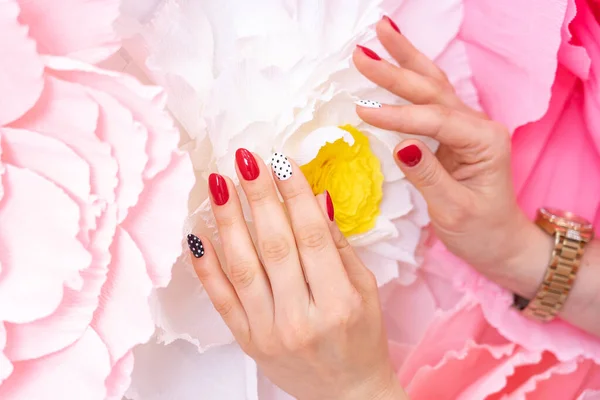 Women 's hands. Multi- colored manicure using red, black and white colors . Three nails painted red. The nail on index finger is white with black polka dots . On little finger black white polka dots